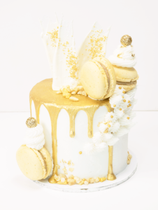 Oh My Cake's "Golden Moment" cake, which is a white buttercream cake, dripping in gold and topped with golden macaroons and white chocolate shards