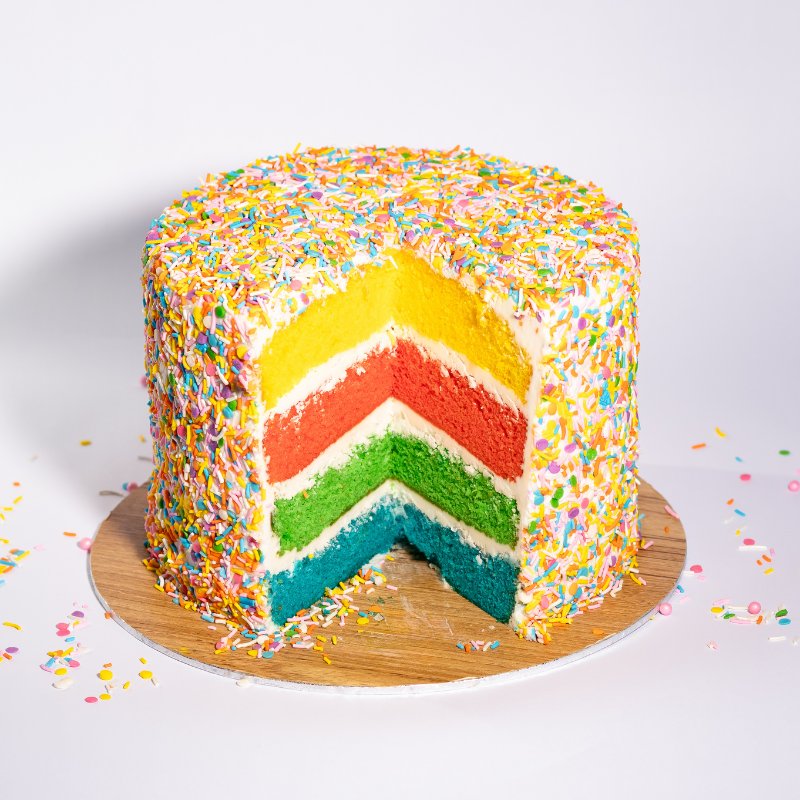 rainbow cake with a slice cut out. the sponges are also rainbow featuring a yellow, red, green and blue sponge