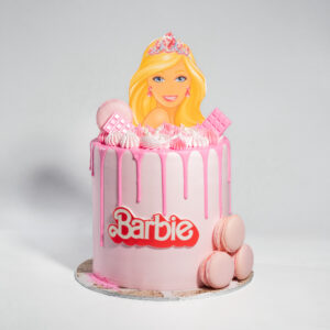 Barbie Inspired Cake with pink drip icing, Barbie topper, macarons, chocolate decorations, and Barbie logo.