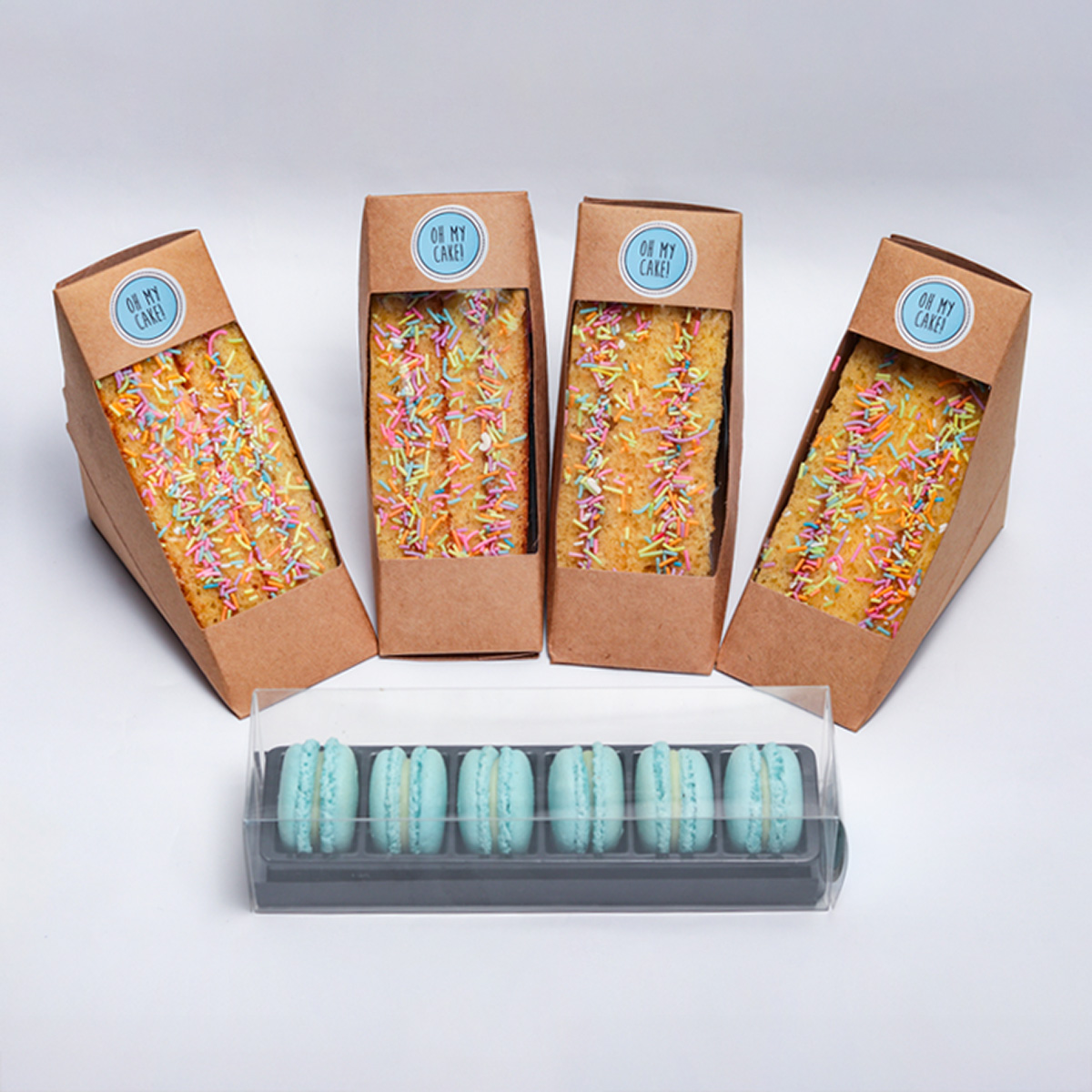 The Sweet selection Platter featuring four kraft boxes of decorated cakes with sprinkles and a container of blue macarons from Oh My Cake