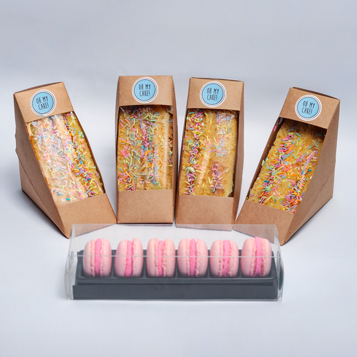 The Sweet selection Platter featuring four kraft boxes of decorated cakes with sprinkles and a container of pink macarons from Oh My Cake