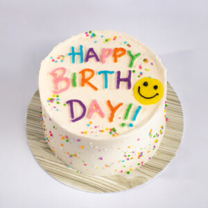 Confetti Mood cake with creamy white frosting, colourful “HAPPY BIRTHDAY DAY!!” lettering, sprinkles, and a yellow smiley face decoration.