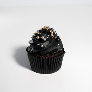 Sparkle Glitz cupcake with black piped swirl frosting, decorated with pearl-like beads and gold sprinkles, set against a white background.