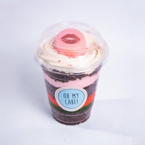 Gourmet chocolate cup dessert in a clear plastic cup, featuring layered dark and light cream filling, topped with a pink kiss-mark decoration and labeled “OH MY CAKE!”.