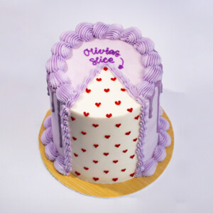 Slice Slice cake with lavender piped frosting, white top surface with red heart sprinkles, and “Olivia’s slice” text on top.