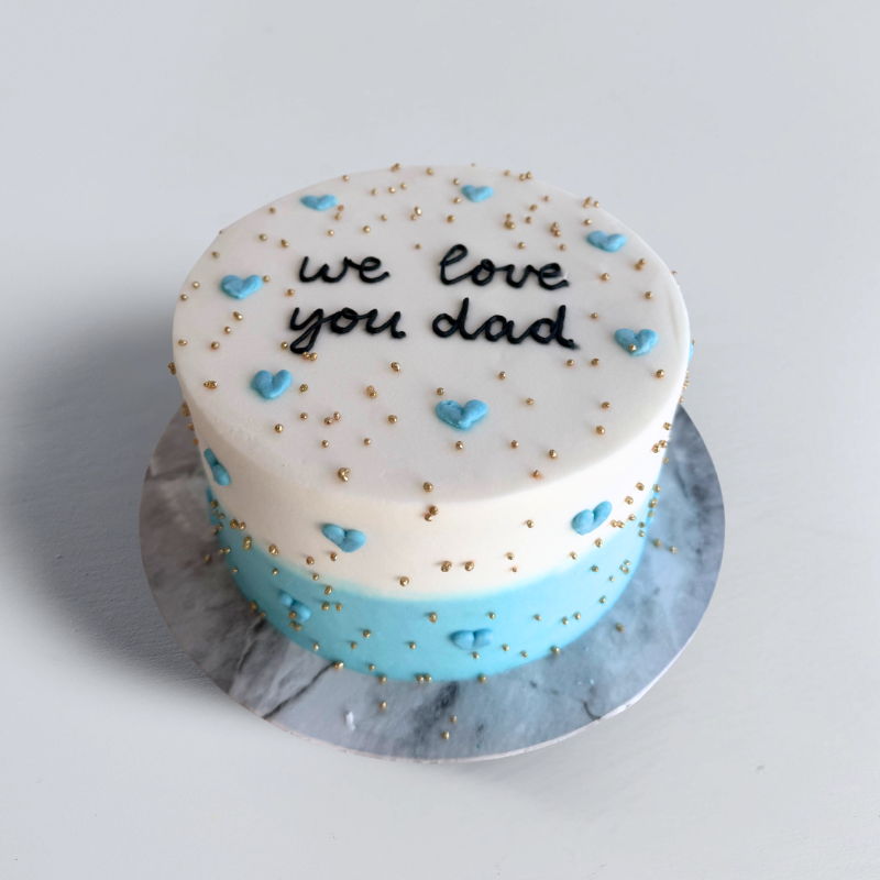 Lifetime of Love Cake with white and blue icing, "We Love You Dad" message, blue hearts, and gold pearl decorations.