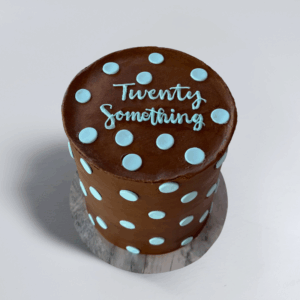 Polka Dot chocolate birthday cake with light blue polka dots and “Twenty Something” lettering on a marble-patterned cake board.