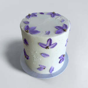 Pretty Petals white cake decorated with delicate purple flowers, scattered petals and gold sugar pearls.