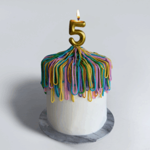 Silly String Inspired birthday cake with colourful blue, pink, yellow and purple icing loops and a gold number 5 candle on a marble cake board.